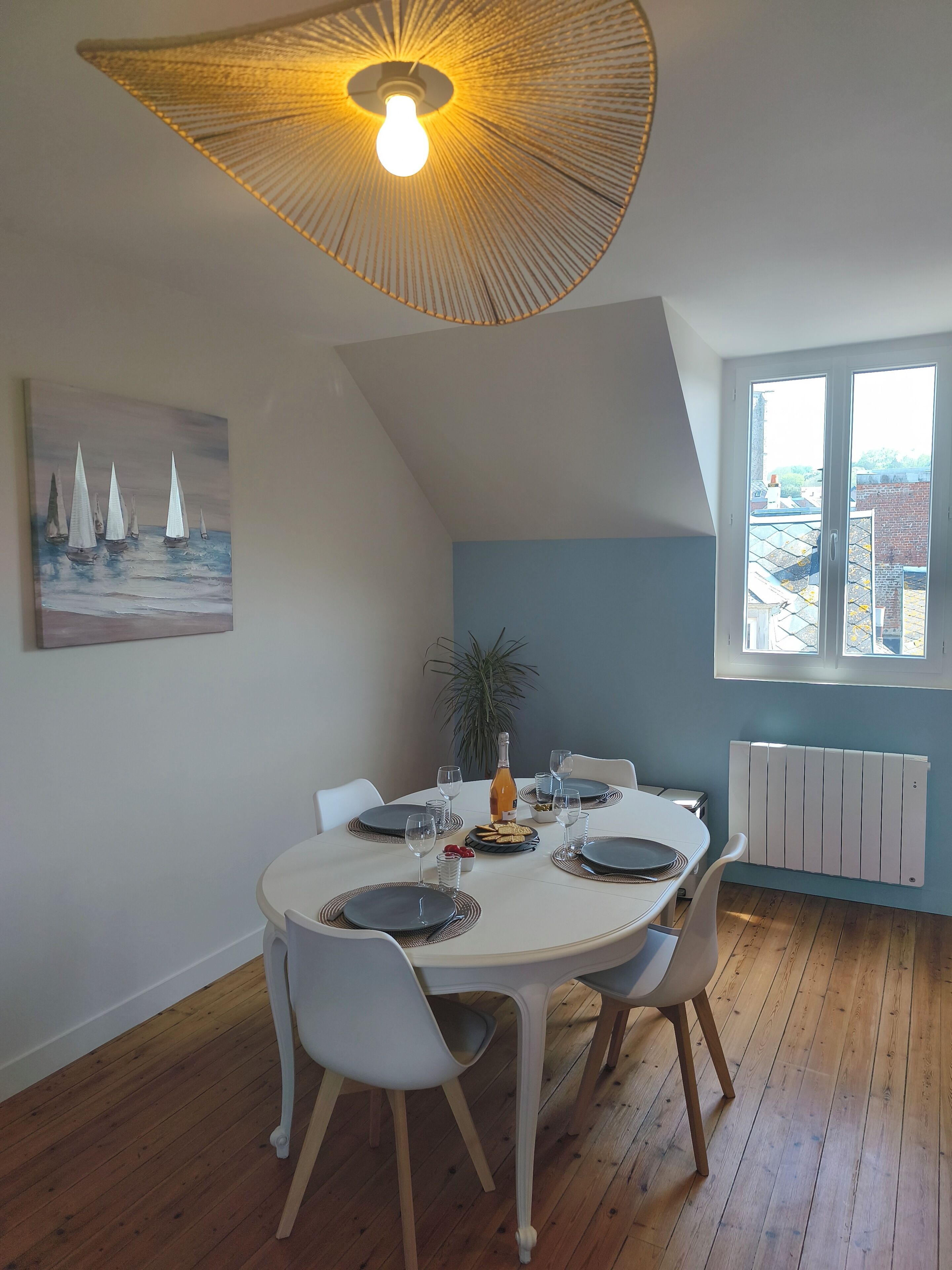 A dining area with a round table, chairs, a bottle of wine, and a painting on the wall.