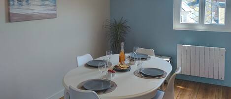 A dining area with a round table, chairs, a bottle of wine, and a painting on the wall.