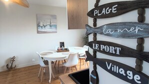 Et spiseområde med et hvidt bord og stole, trægulv og et ophængt skilt med ordene 'PLAGE la mer', 'PORT' og 'Village'.