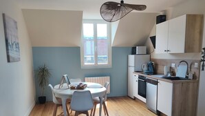 En kompakt opholdsstue med spiseplads, tekøkken og ventilator.