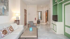 Una sala de estar con sofá, sillón, mesa de centro, mueble para televisión y obras de arte en las paredes.