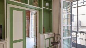 Una habitación con paredes verdes y blancas, un ventanal con vistas al exterior, una silla y una mesita con un florero.