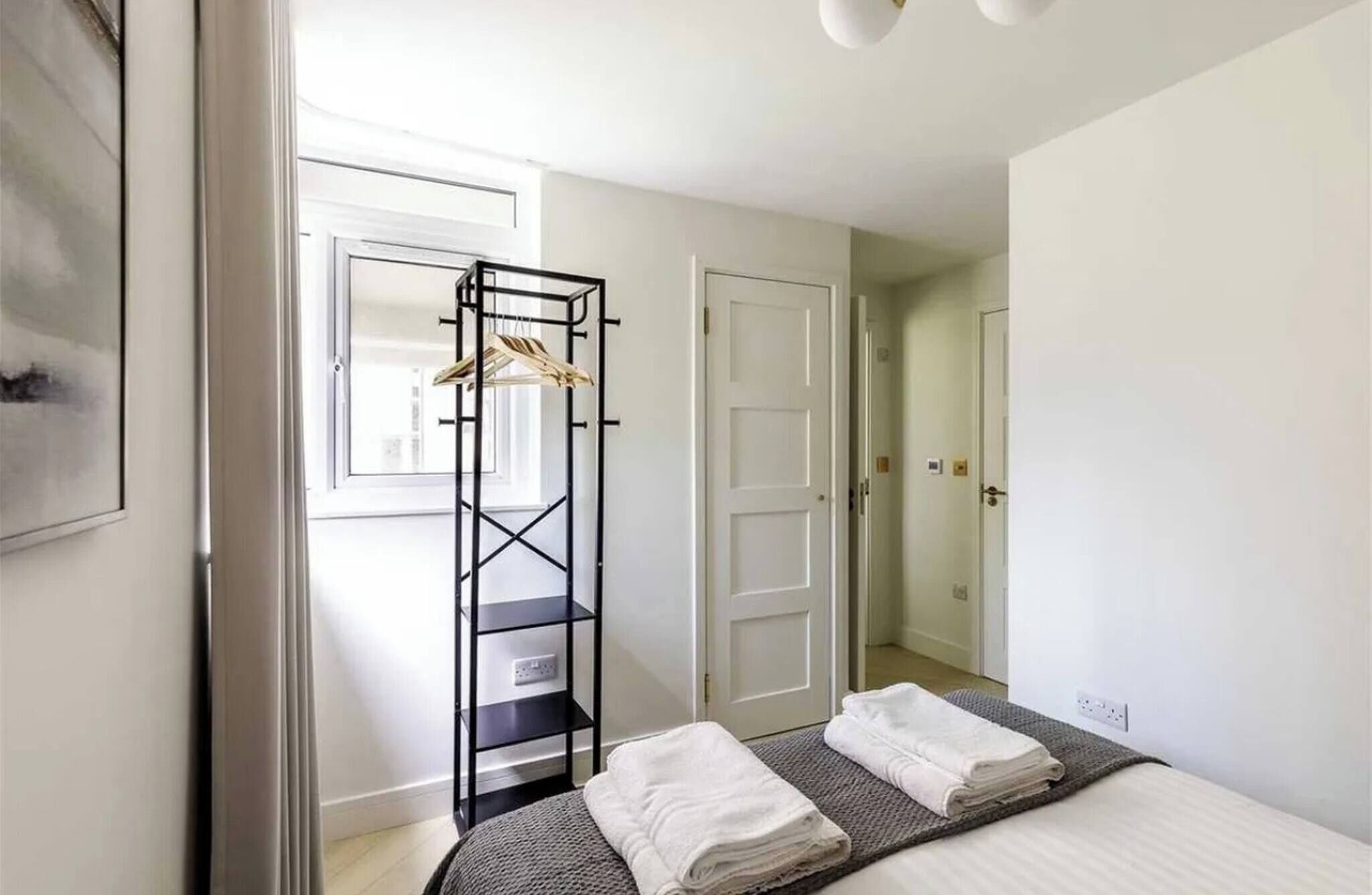 Ein Schlafzimmer mit einem Bett, einem schwarzen Wäscheständer und einer weißen Tür.