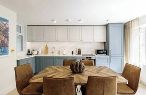 A modern kitchen with light blue cabinets, a wooden dining table, and brown chairs. - Soho 3bedroom Entire Flat - Spacious Sleeps 10 (London)