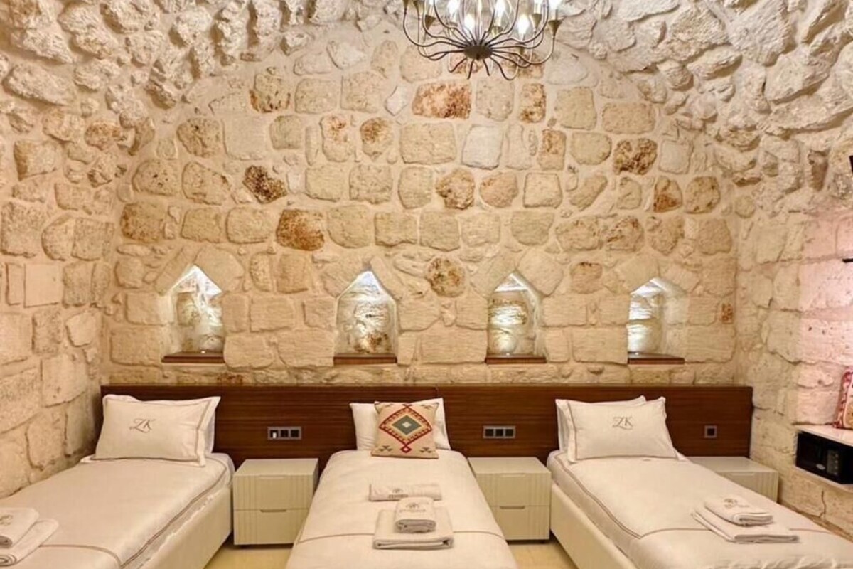 Quarto com parede de pedra, um lustre e três camas.