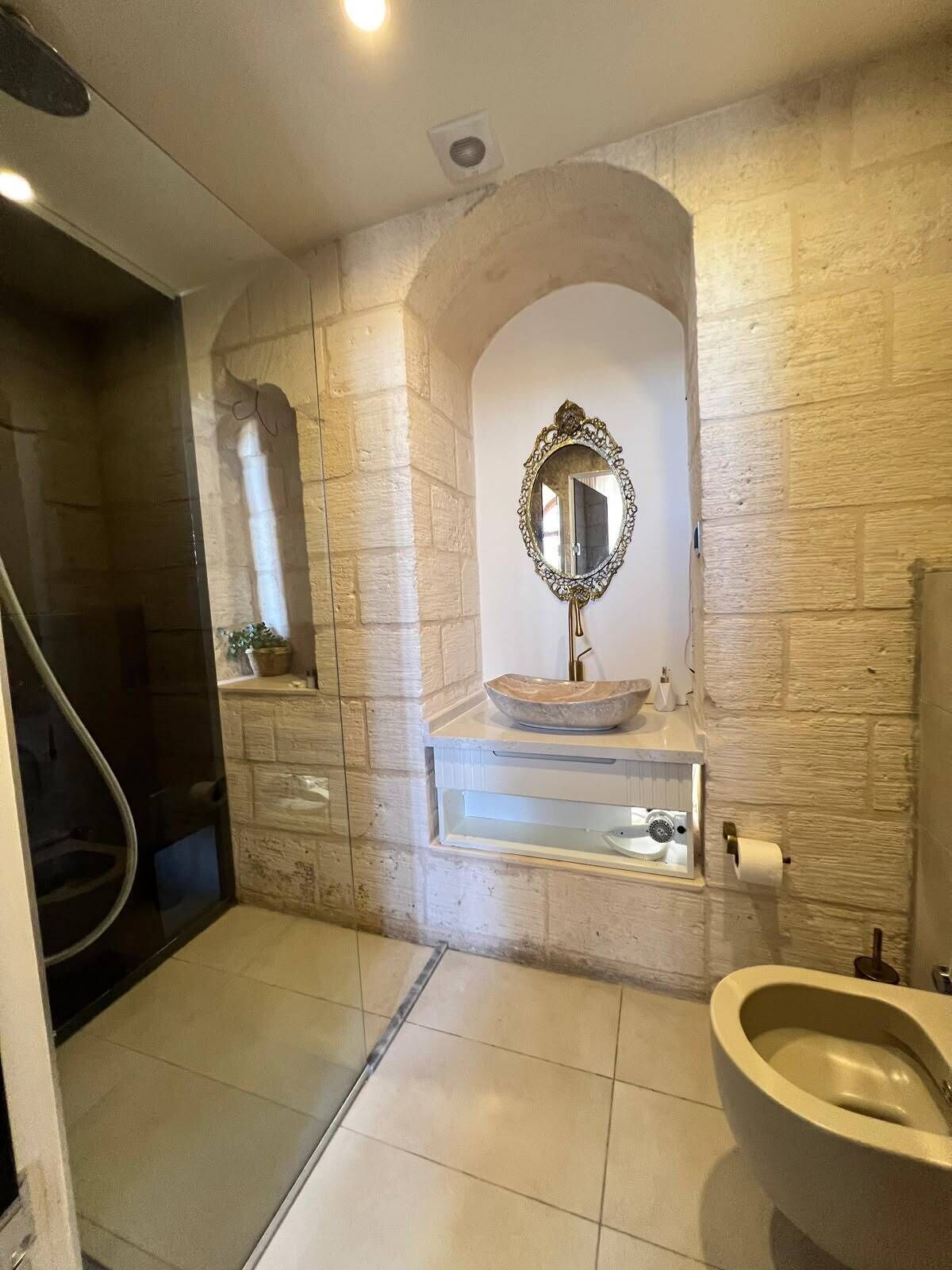 Et badeværelse med stenvæg, vask med marmorvask, spejl og bidet.