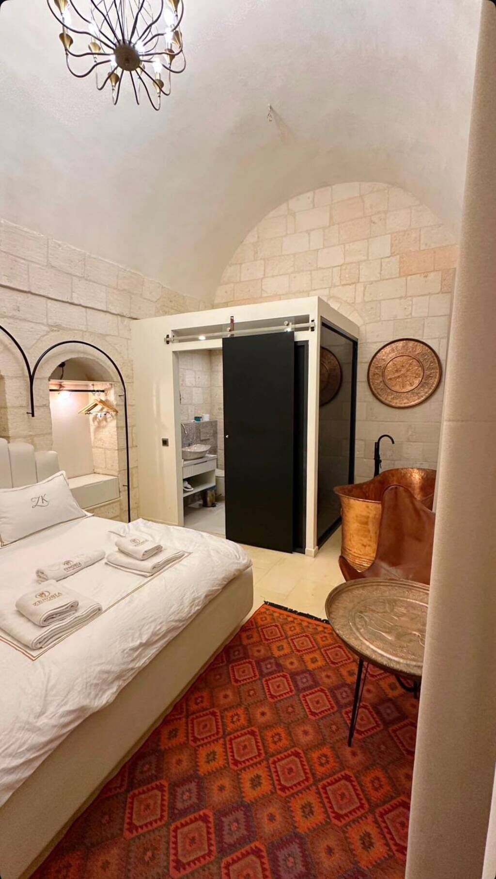 Una habitación de hotel con cama, baño, una mesita y una lámpara de techo original.