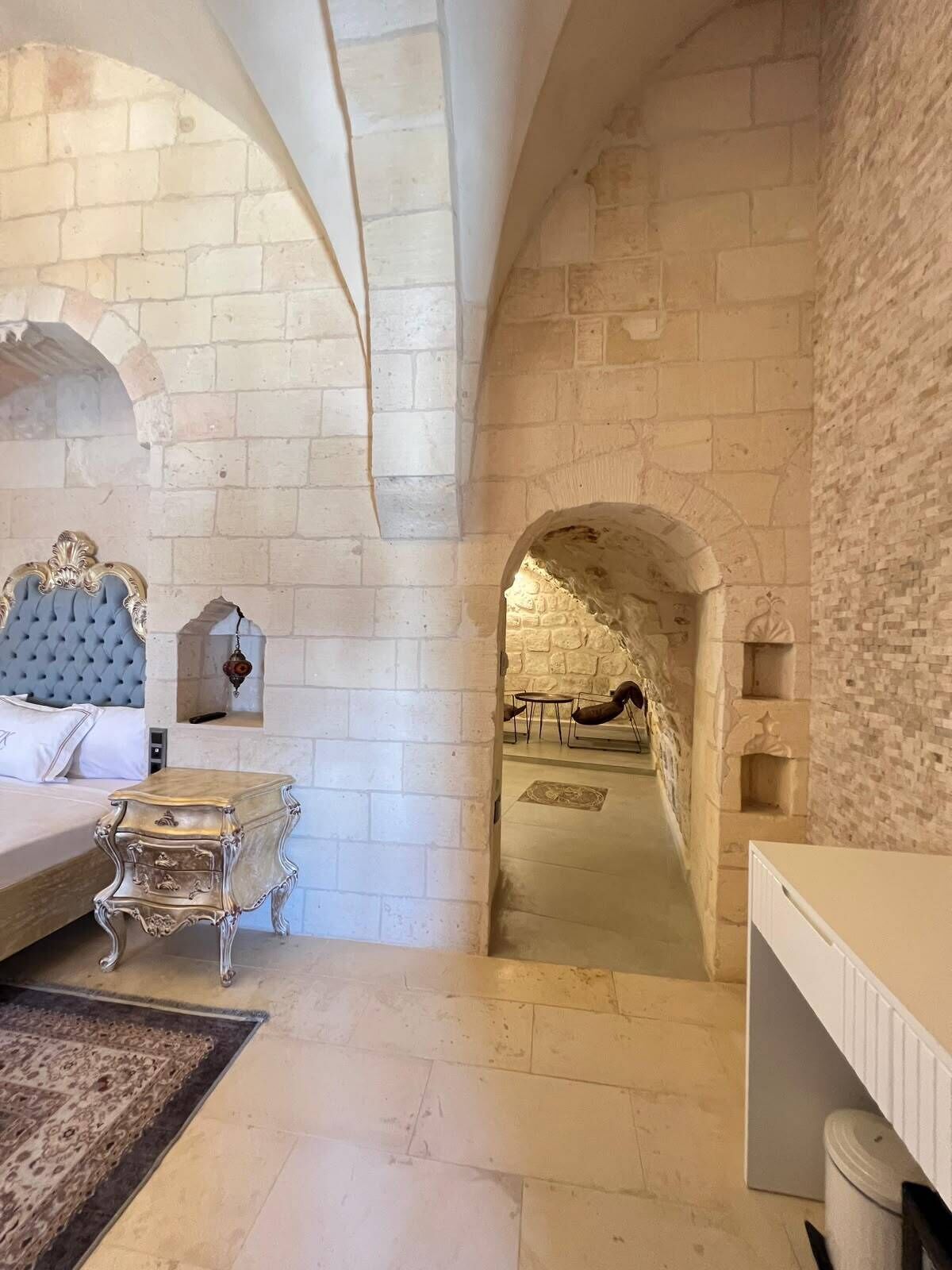 A room with a bed, a nightstand, a dresser, and an arched doorway leading to another room.