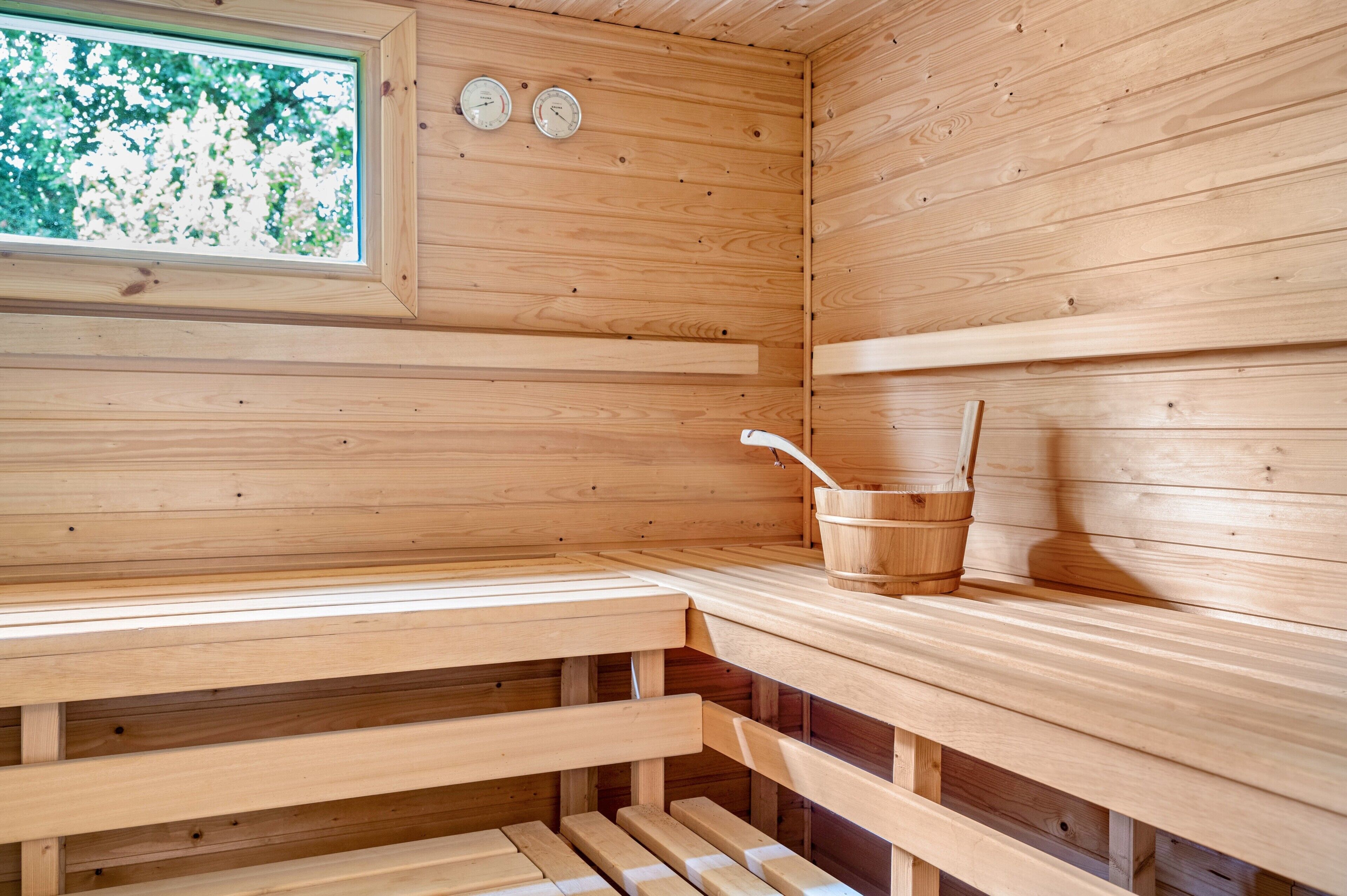 A wooden sauna with benches, a window, and two wall-mounted clocks.