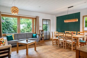 A modern living room with a sofa, coffee table, and dining area with chairs. - Gina's Holiday Home with Garden, Treehouse Terrace and Sauna (Eggstedt)
