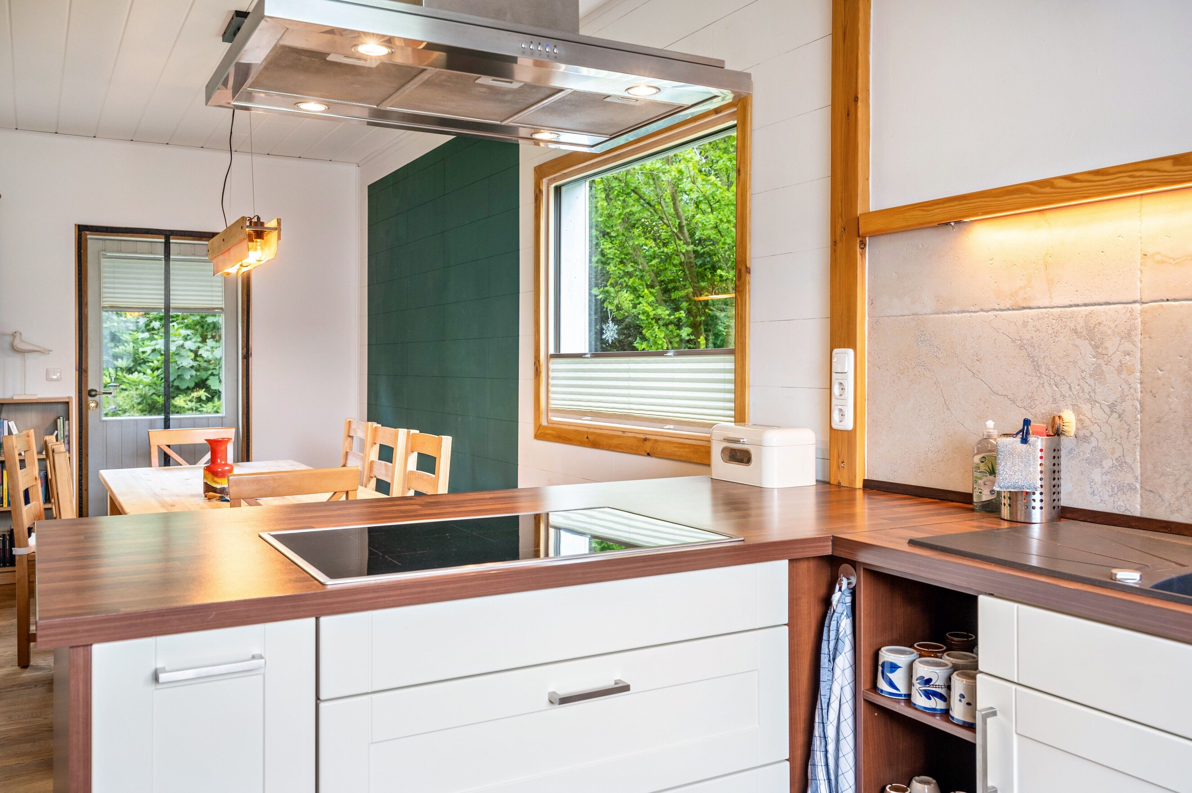 Een moderne keuken met een ingebouwde kookplaat, houten aanrecht en een raam met uitzicht op groen.