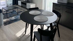 En moderne stue med et rundt bord, to stole, et fjernsyn og et køkkenhjørne.