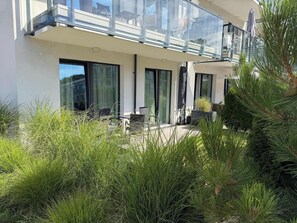 A modern building with a glass balcony, outdoor seating, and lush greenery. - Niechorze Residence - beachfront, pool & free SPA (Niechorze)