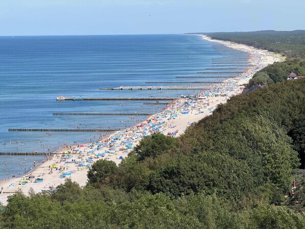 A beach with multiple piers extending into the water, lined with umbrellas and beachgoers.