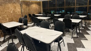 Un comedor con mesas de mármol y sillas negras, ventanas amplias con vistas a la ciudad y suelo de mármol.