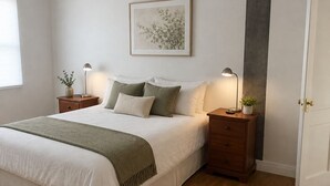 Un dormitorio con cama, mesitas de noche, ventilador de techo, un cuadro enmarcado y una puerta.