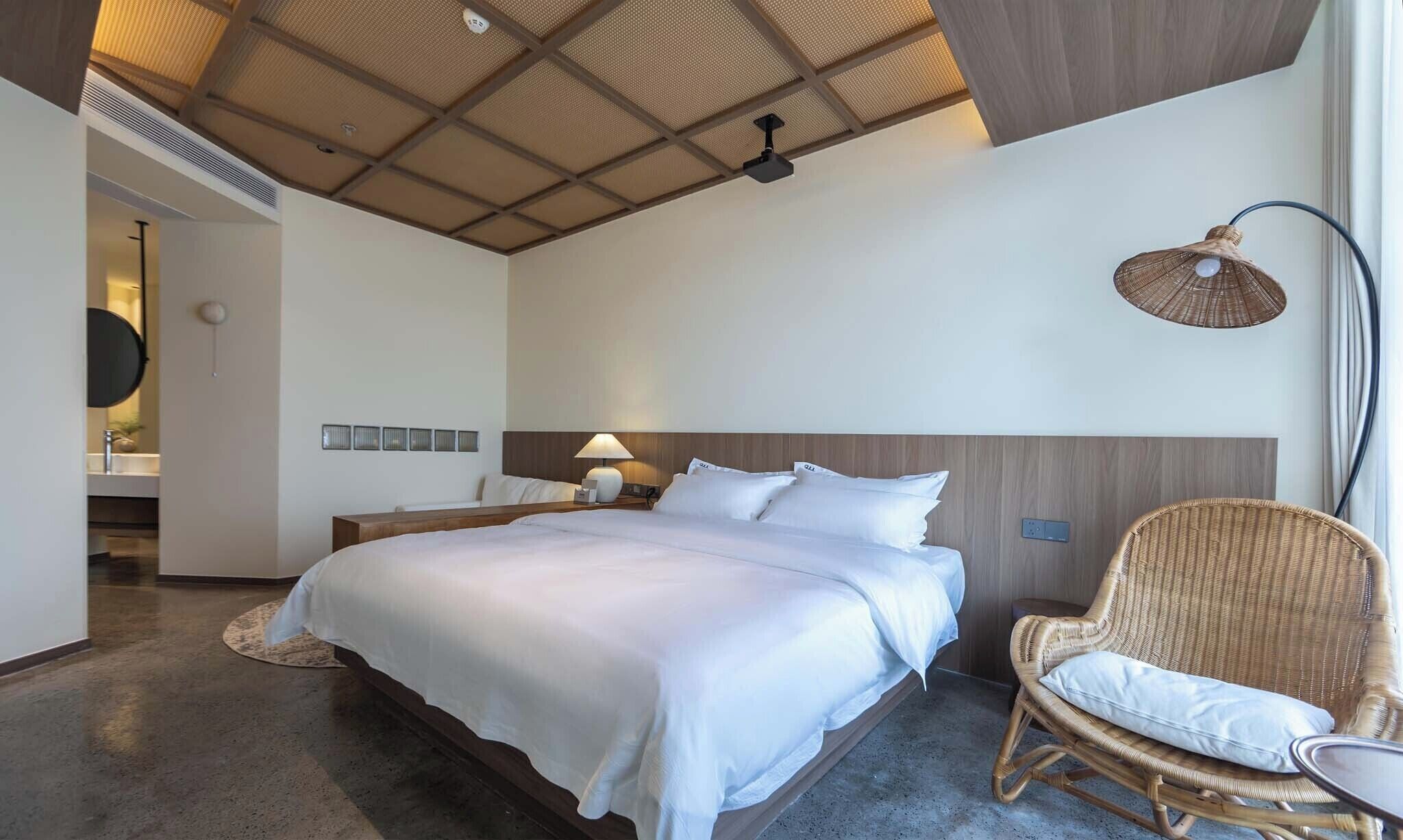 Habitació d'hotel moderna amb un llit gran, una taula de nit, una cadira i un ventilador de sostre.
