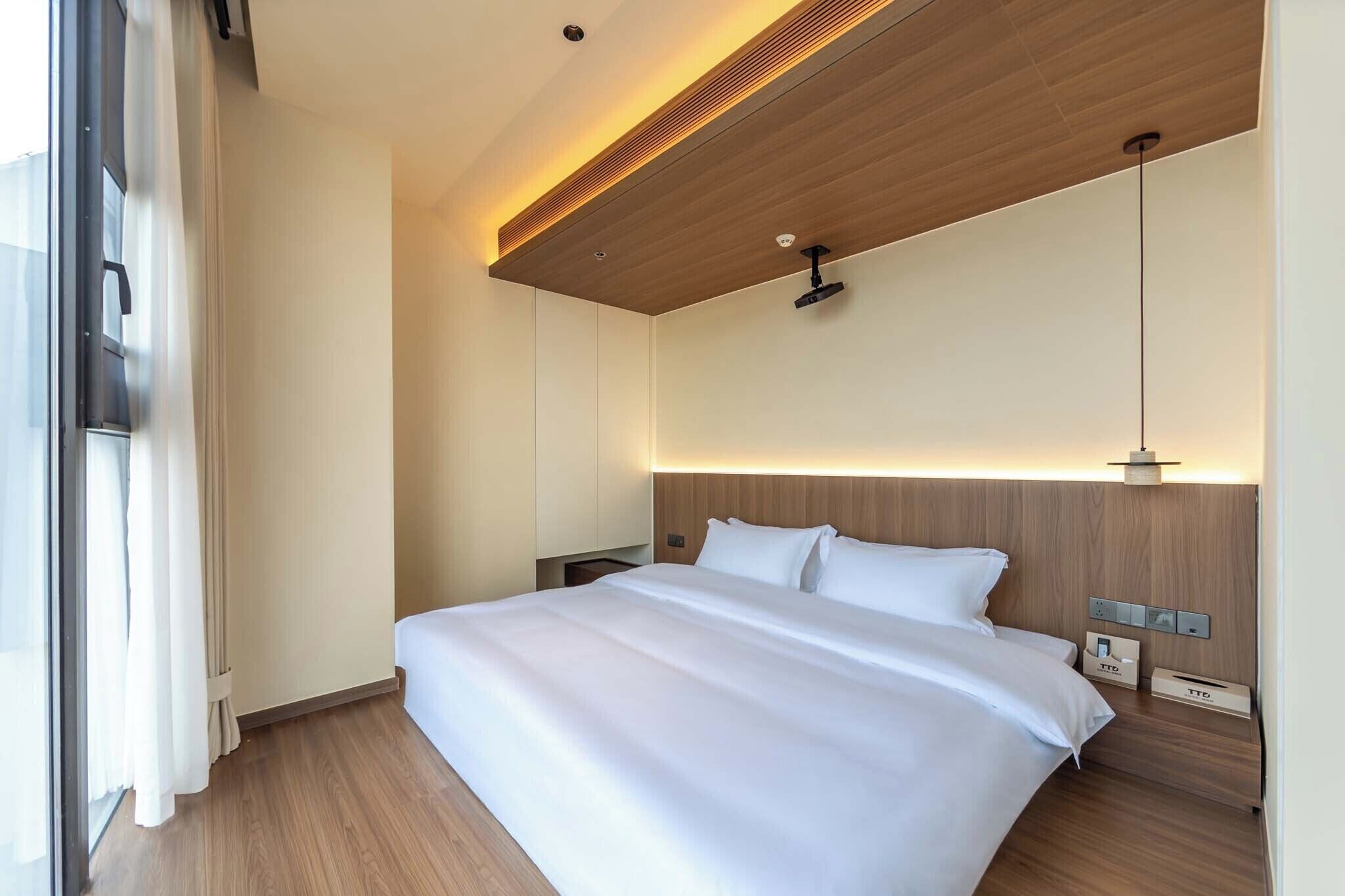 Ein modernes Hotelzimmer mit einem großen Bett, einem Holz-Kopfteil und einer Deckenleuchte.