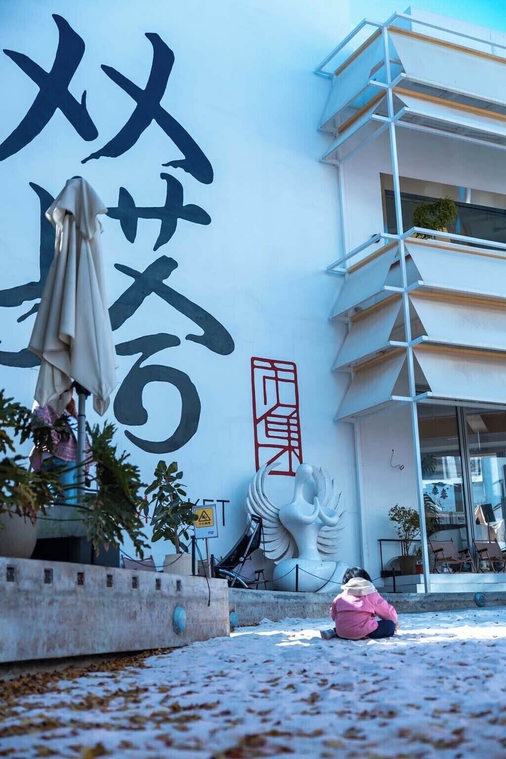 Een gebouw met een grote muur waarop Japanse karakters, een sculptuur en terras zitten.