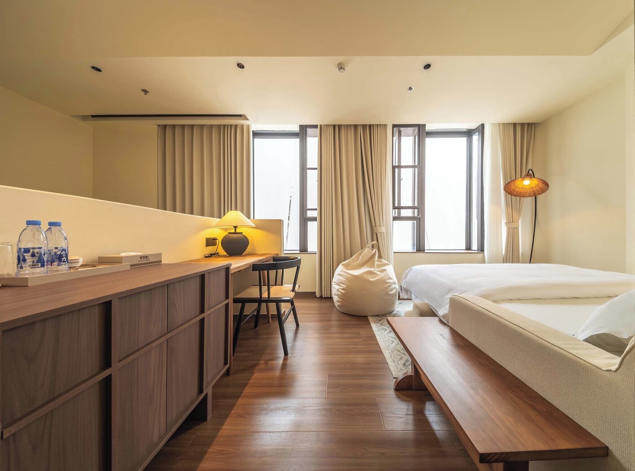 Habitación de hotel con cama, escritorio con lámpara, silla, sillón de peluche y una mesita con botellas de agua.
