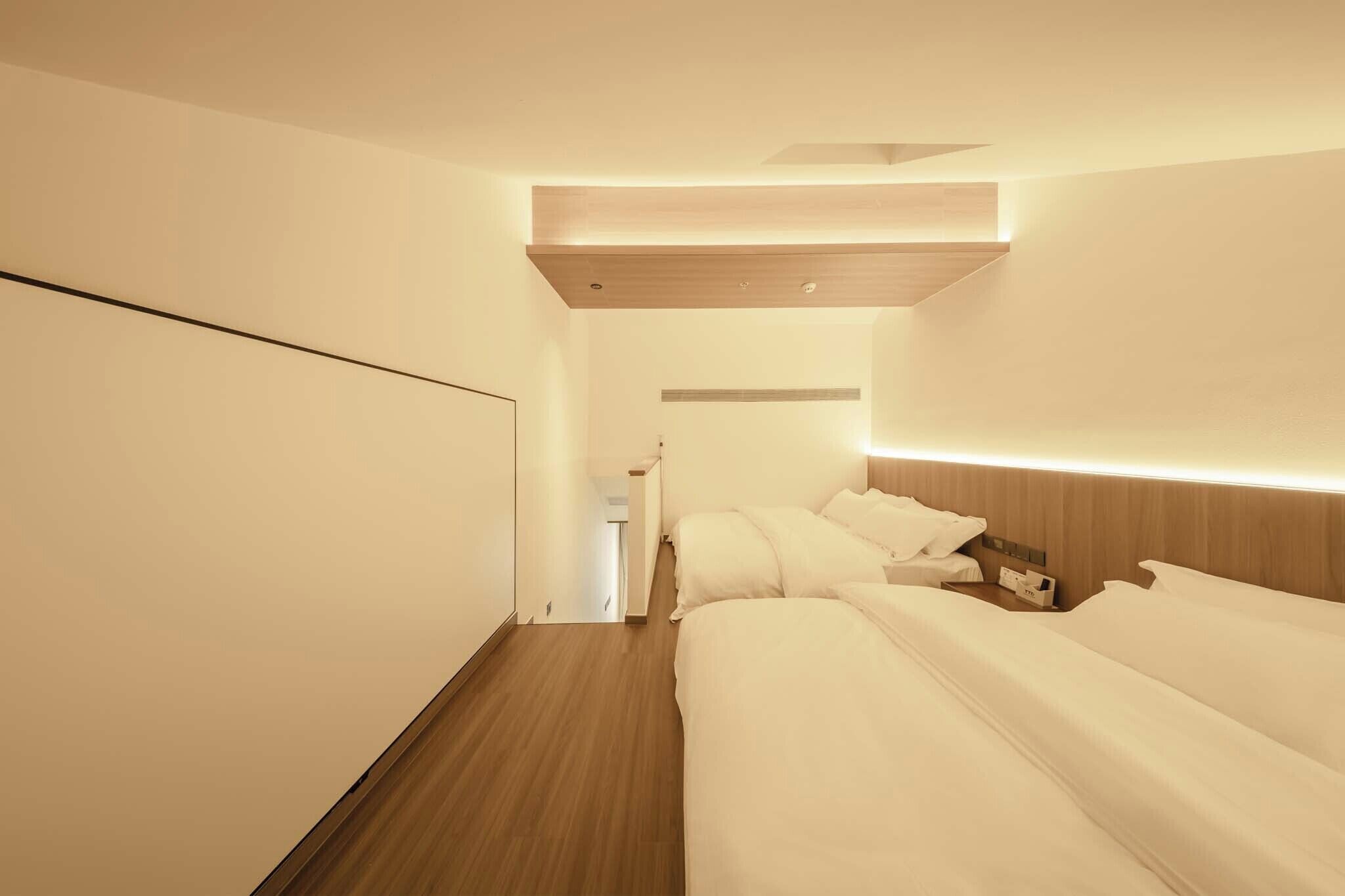 Une chambre d’hôtel avec un plancher en bois, un lit avec une literie blanche, une table de chevet et un luminaire fixé au mur.