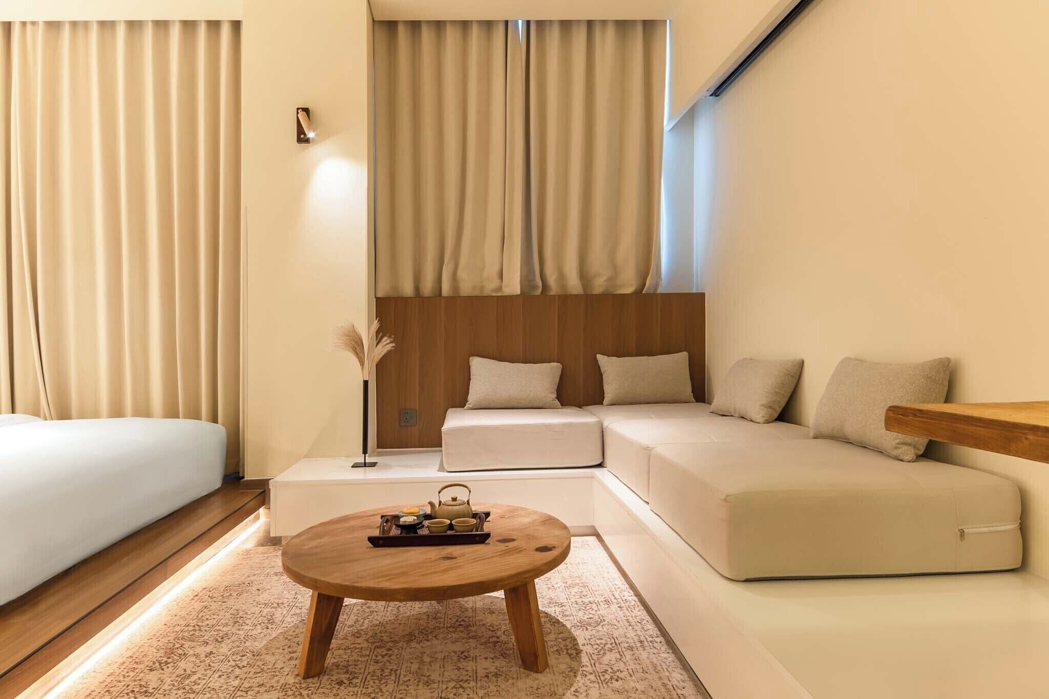 A modern hotel room with a sofa, a wooden coffee table, and a bedside table.