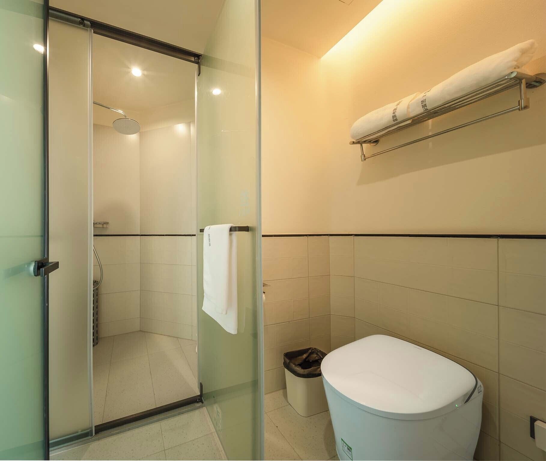 A bathroom with a glass shower enclosure, a toilet, and a towel rack.