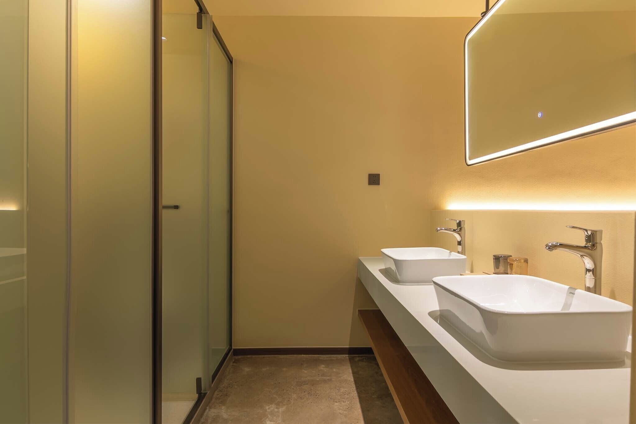 A modern bathroom with a glass shower enclosure, two sinks, and a large mirror.