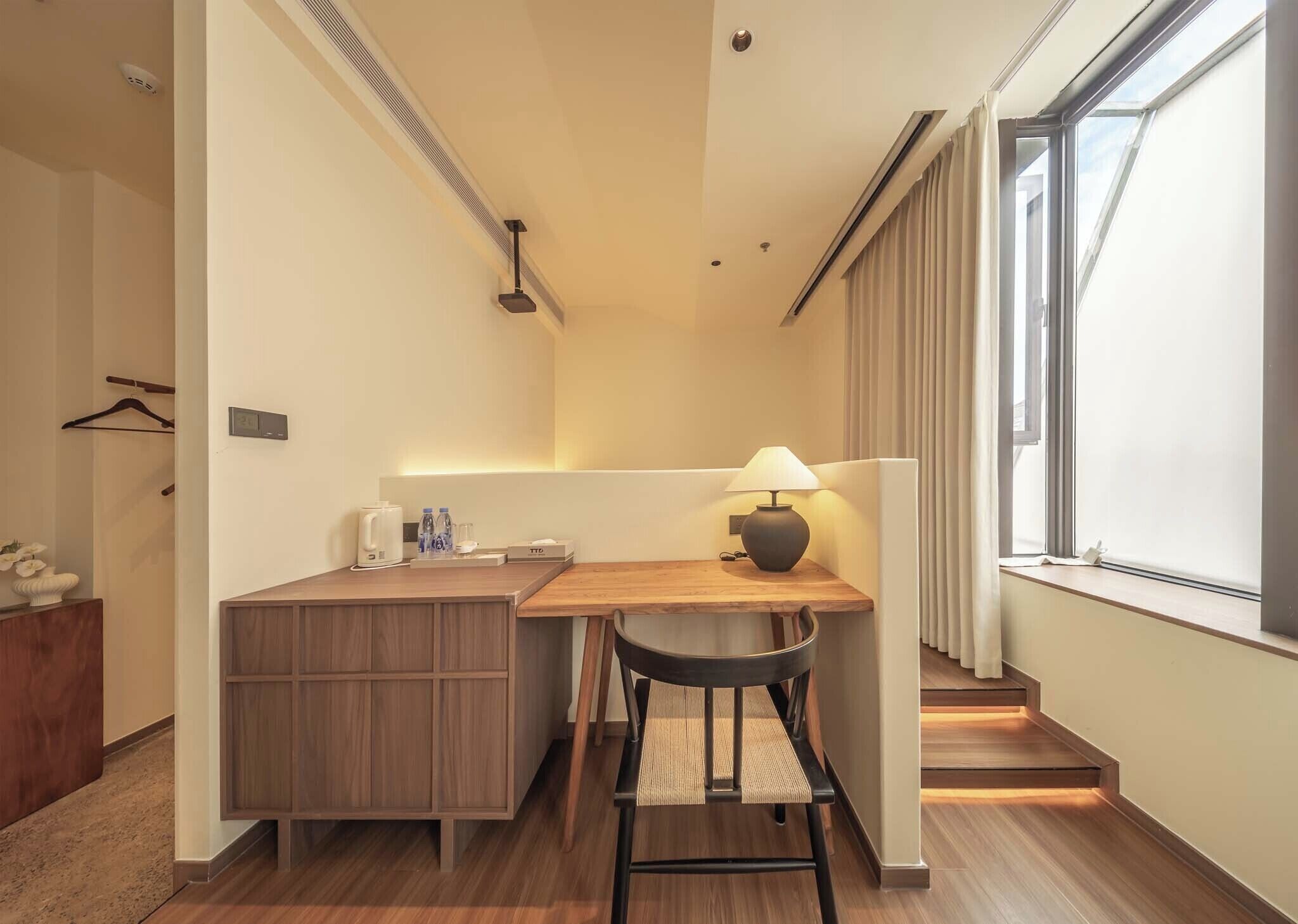 Una habitación de hotel pequeña con kitchenette, un escritorio y una silla, una ventana con cortinas y una escalera.