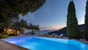 A swimming pool with lounge chairs, surrounded by trees and overlooking a mountainous landscape.