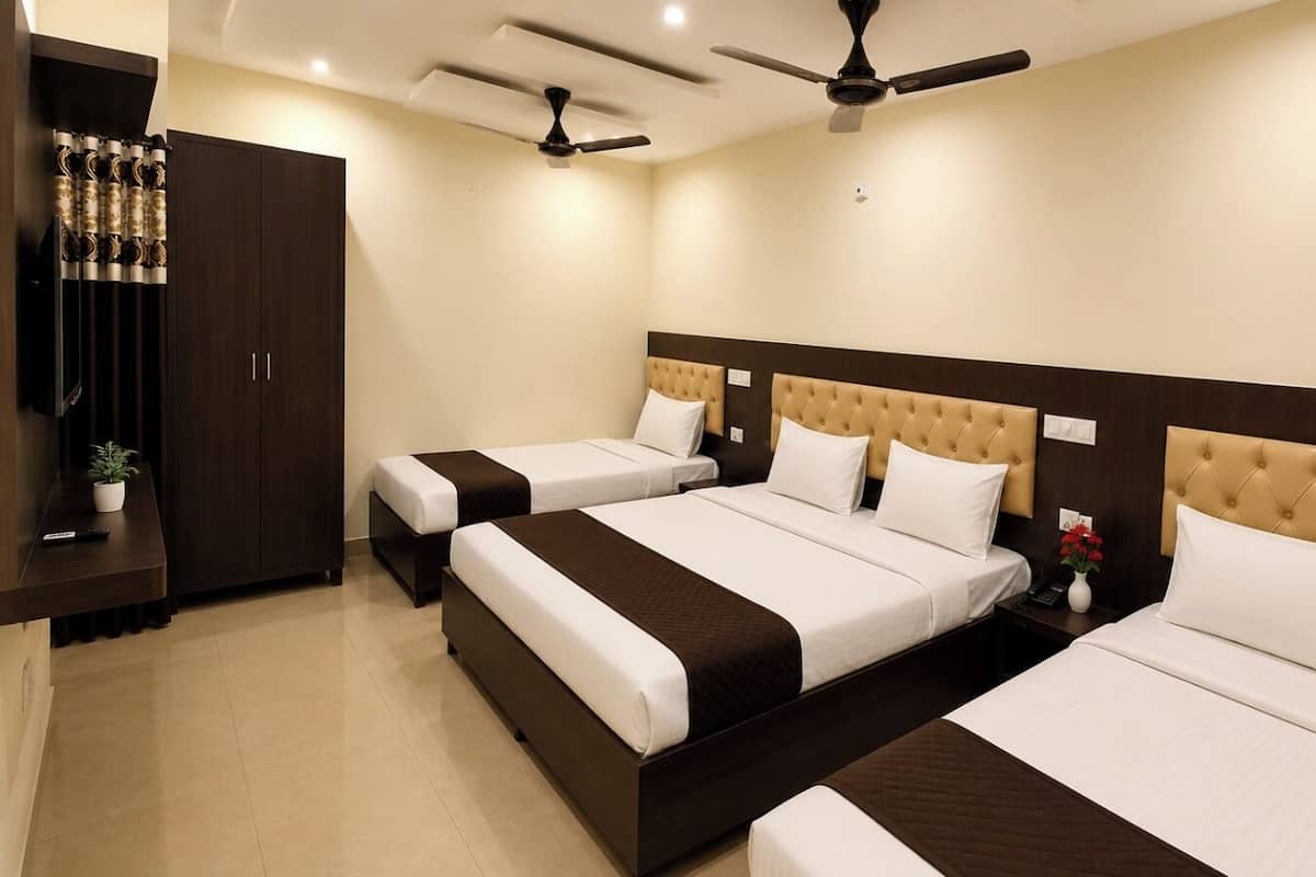 A hotel room with three beds, a dark wooden wardrobe, ceiling fans, and a small table with a plant.