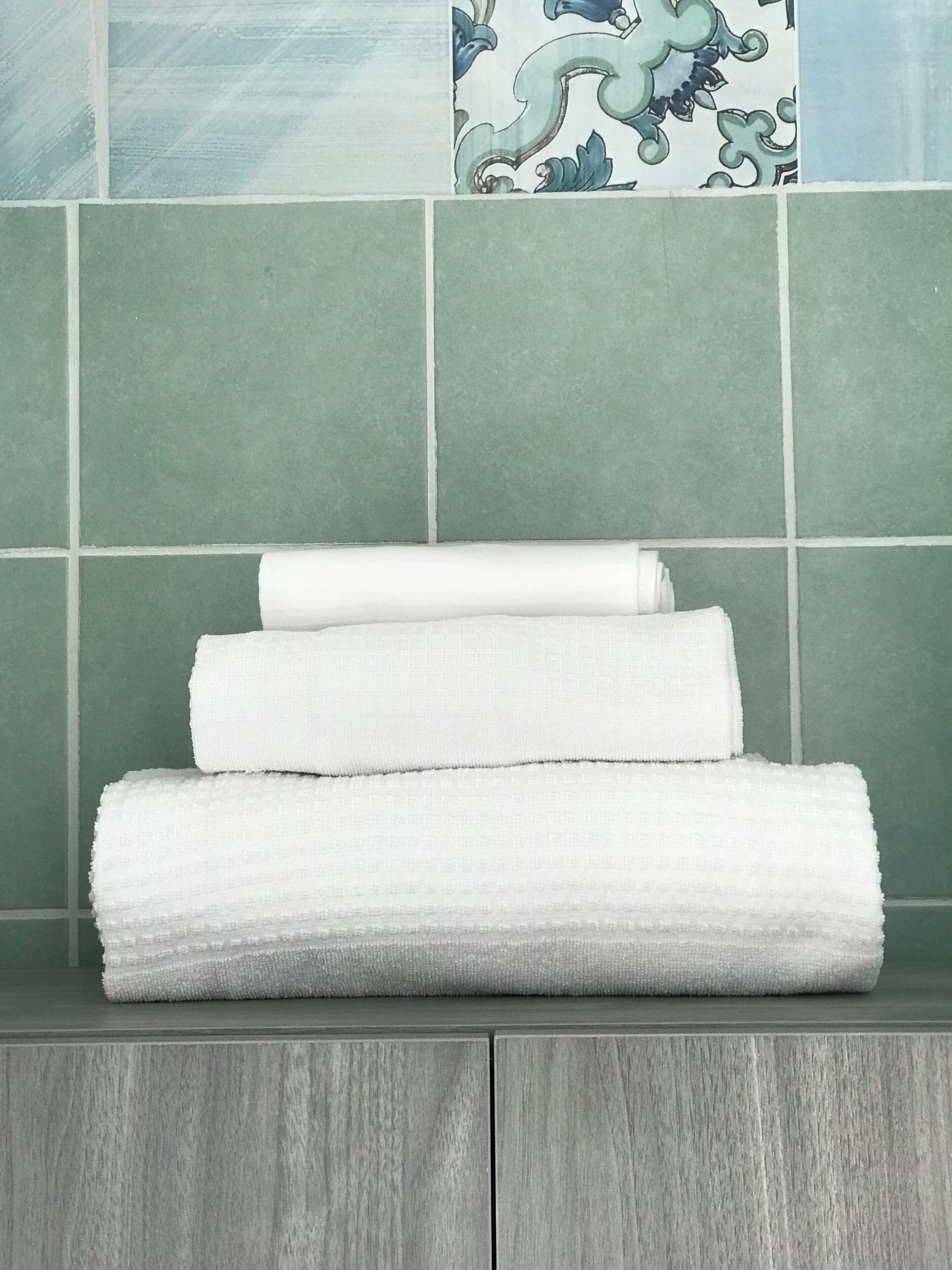 Une pile de serviettes blanches est posée sur une surface en bois, avec des carreaux verts en arrière-plan.