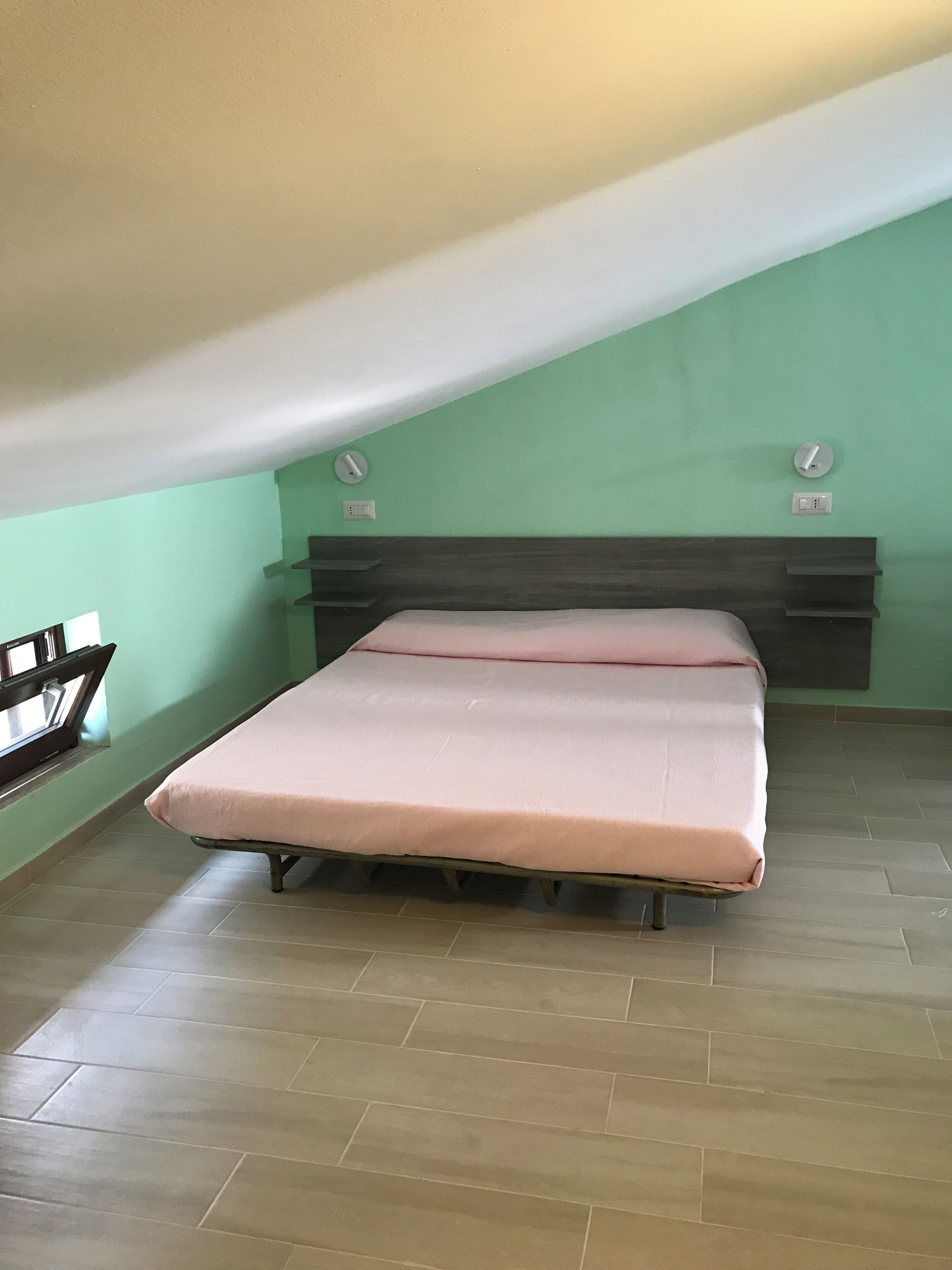 A bedroom with a bed, a window, and a wall-mounted light fixture.