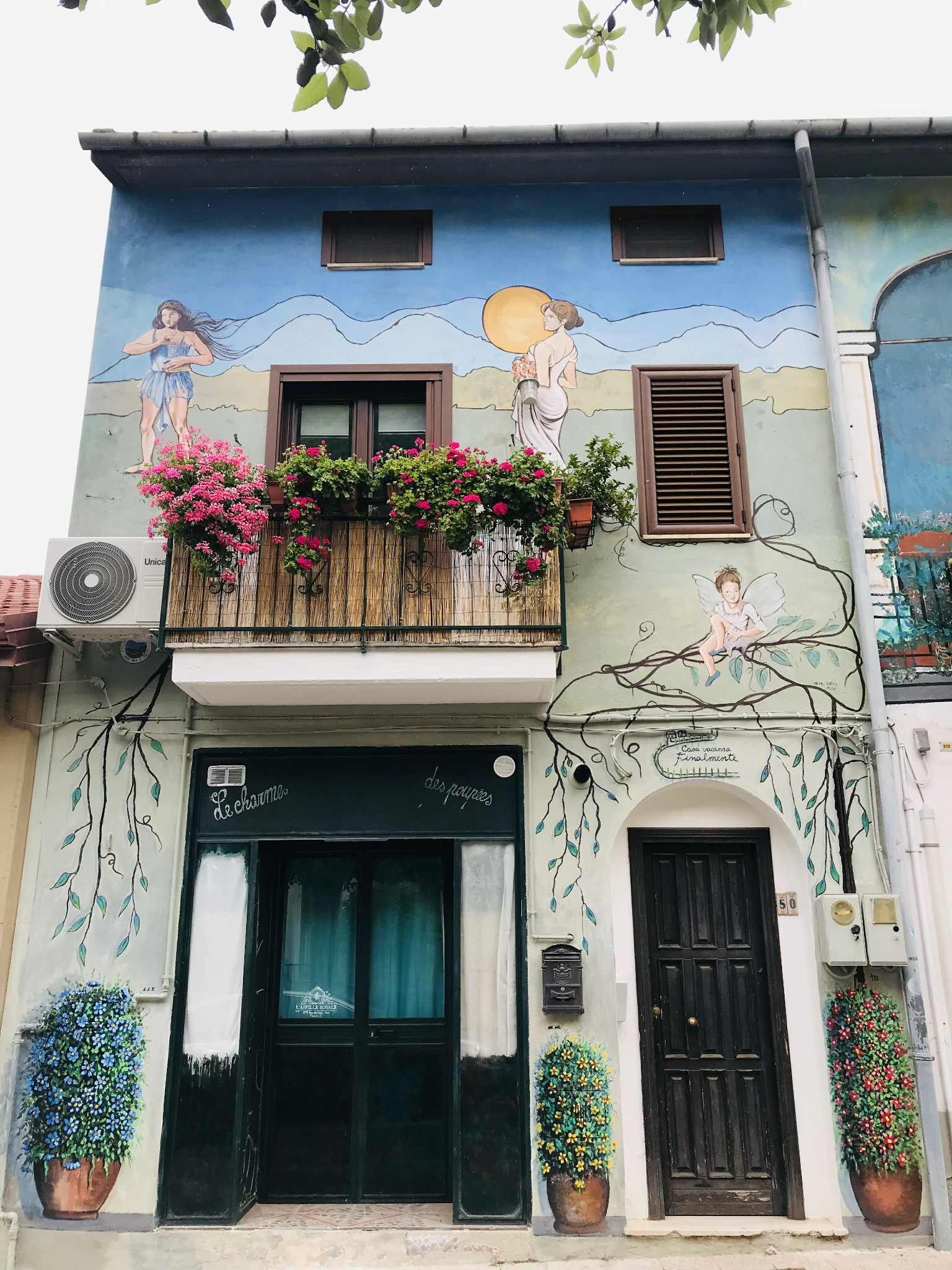 Ein Gebäude mit Wandmalerei, einem Balkon mit Blumen und einer schwarzen Tür.