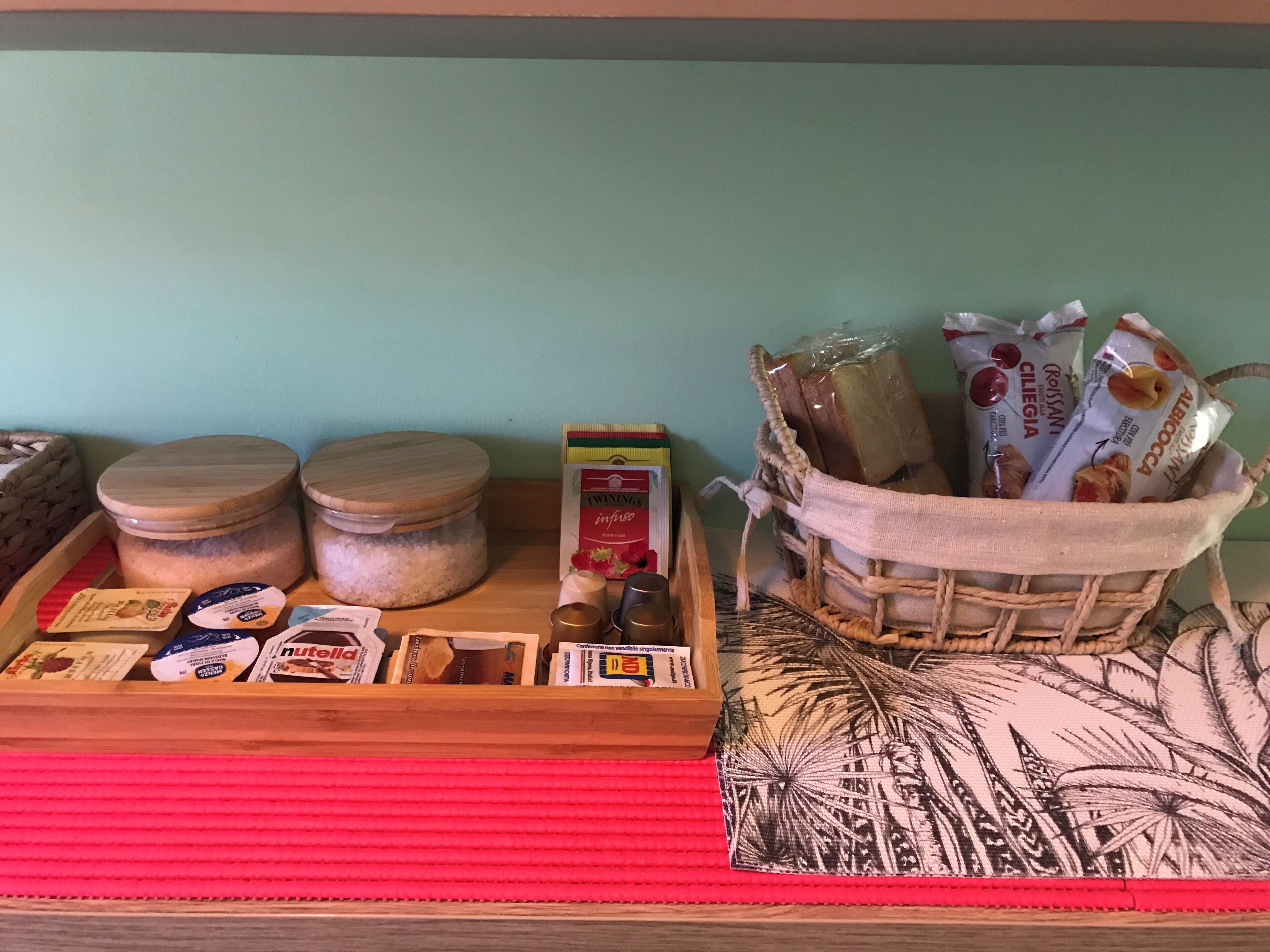Una bandeja de madera con frascos, una caja de té Twinings y una cesta con pan y aperitivos.