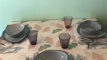 A dining table with plates, glasses, and cutlery set on a tablecloth with a leaf pattern.