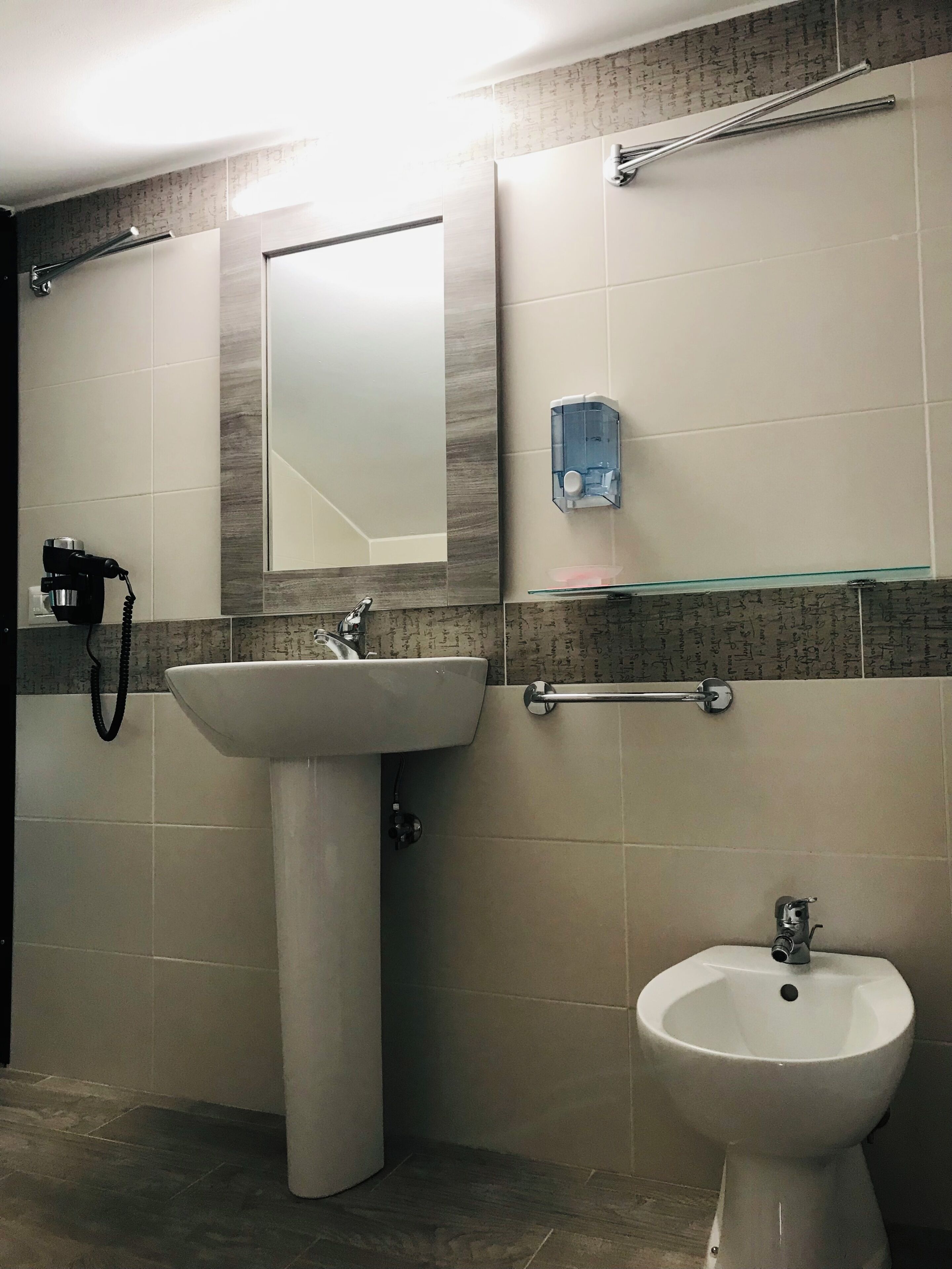 A bathroom with a pedestal sink, a wall-mounted mirror, a handheld hair dryer, and a bidet.