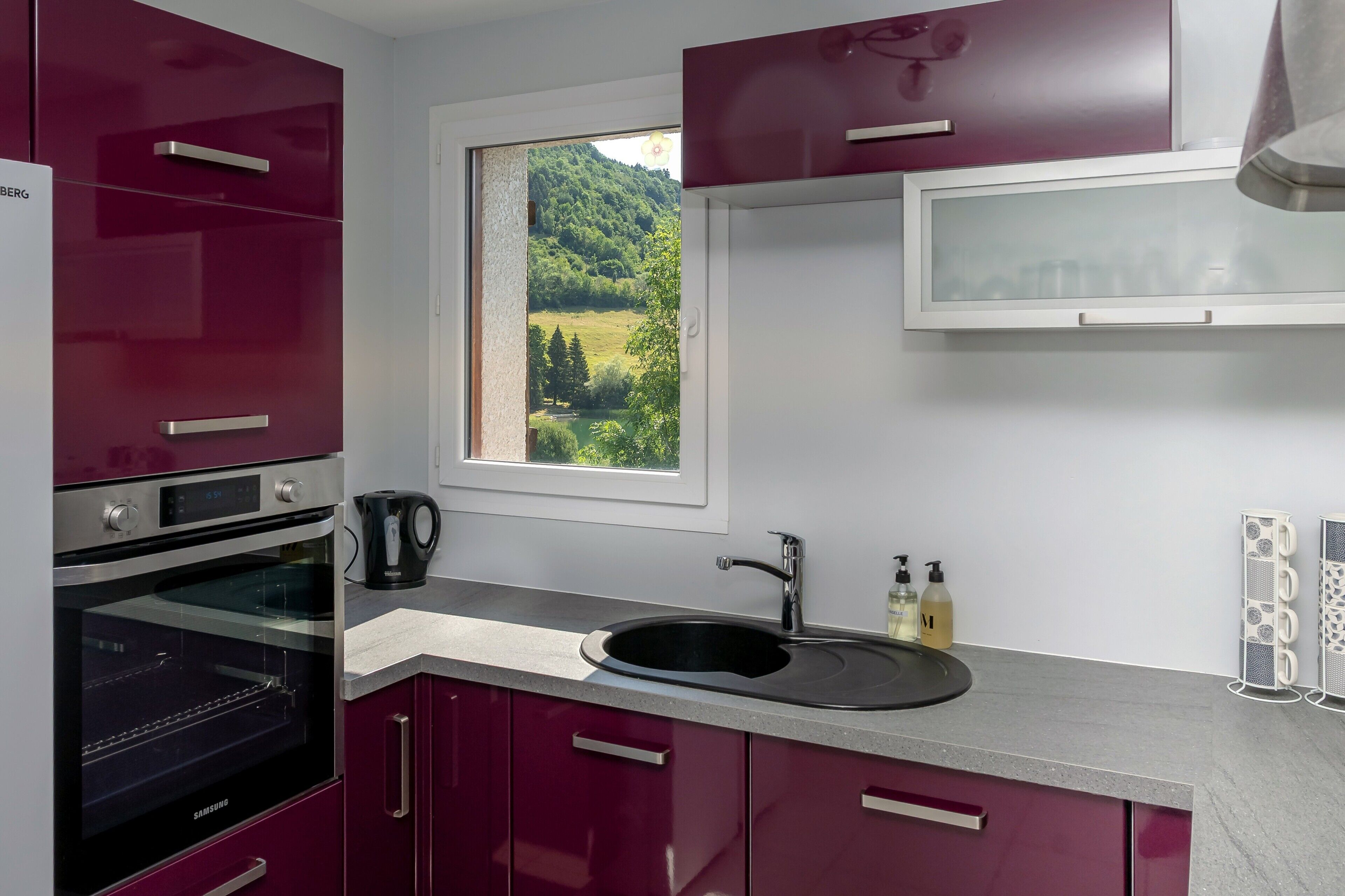 Eine moderne Küche mit Backofen, Spüle und einem Fenster mit Blick auf eine grüne Landschaft.