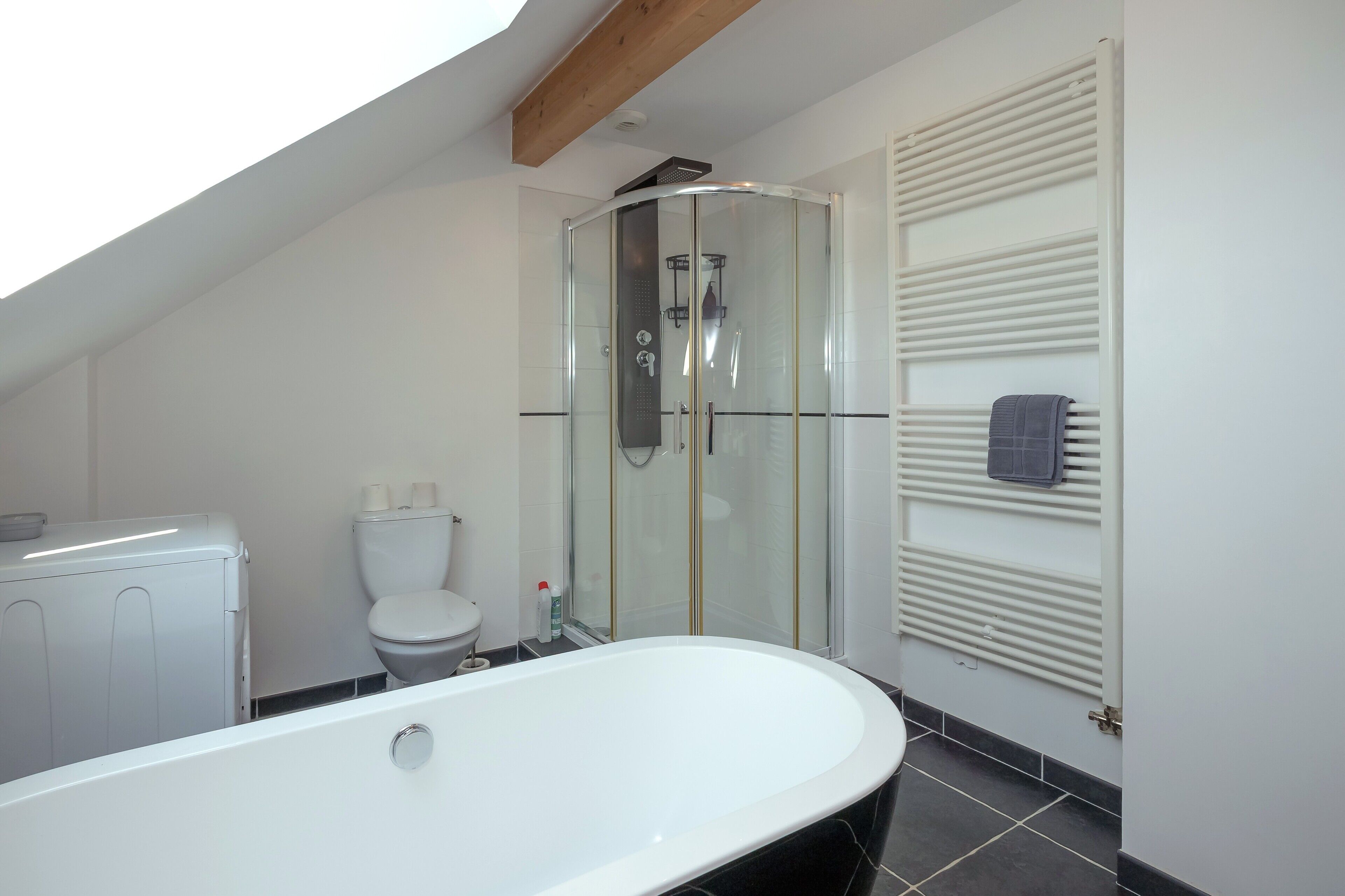 Een moderne badkamer met een douchecabine van glas, een witte badkuip en een toilet.