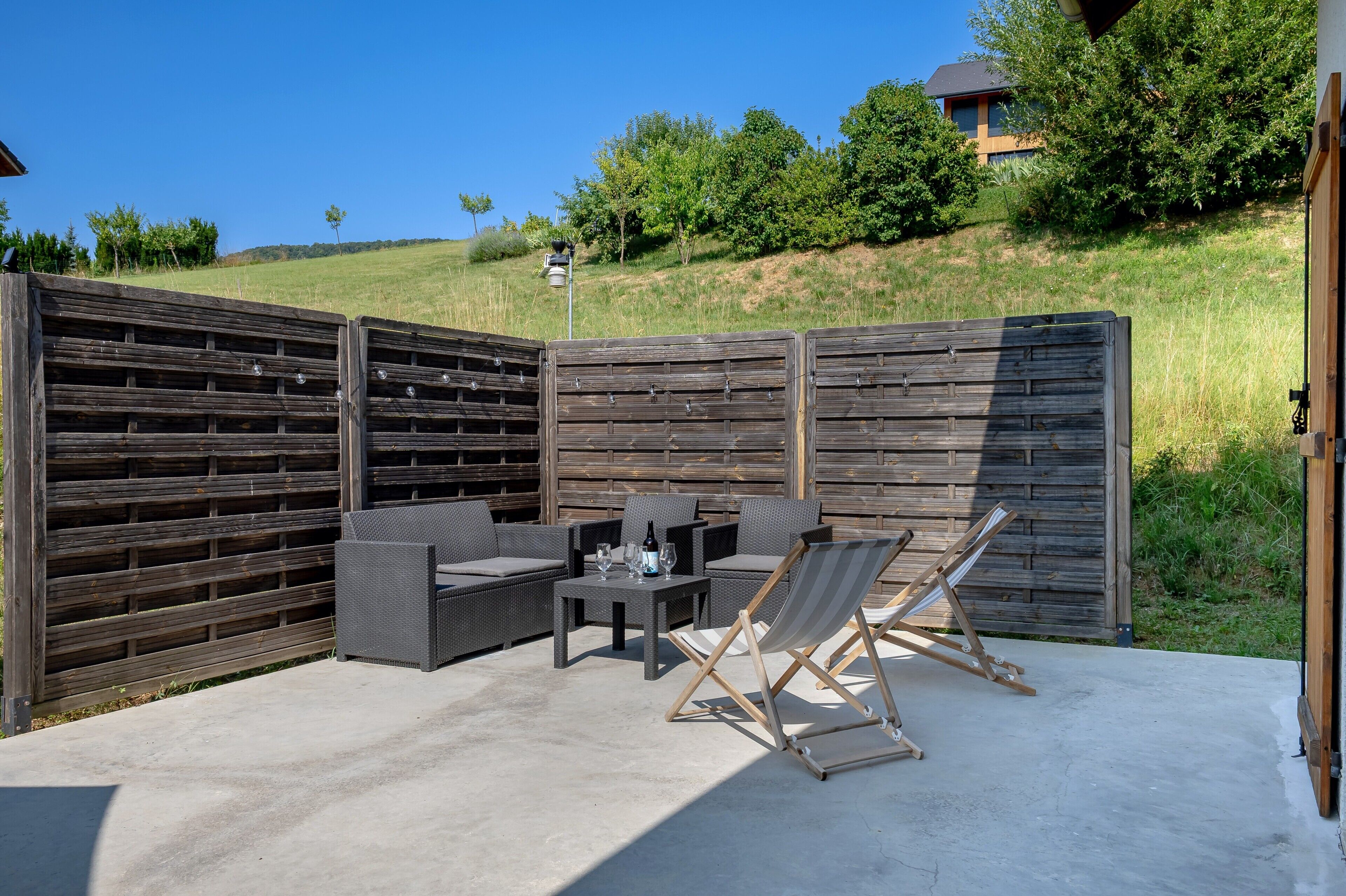 Una terrazza esterna con recinzione in legno, un tavolo con sedie e una poltrona da relax.