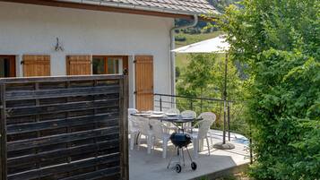 A patio with a table and chairs, a barbecue grill, and a view of a green landscape.