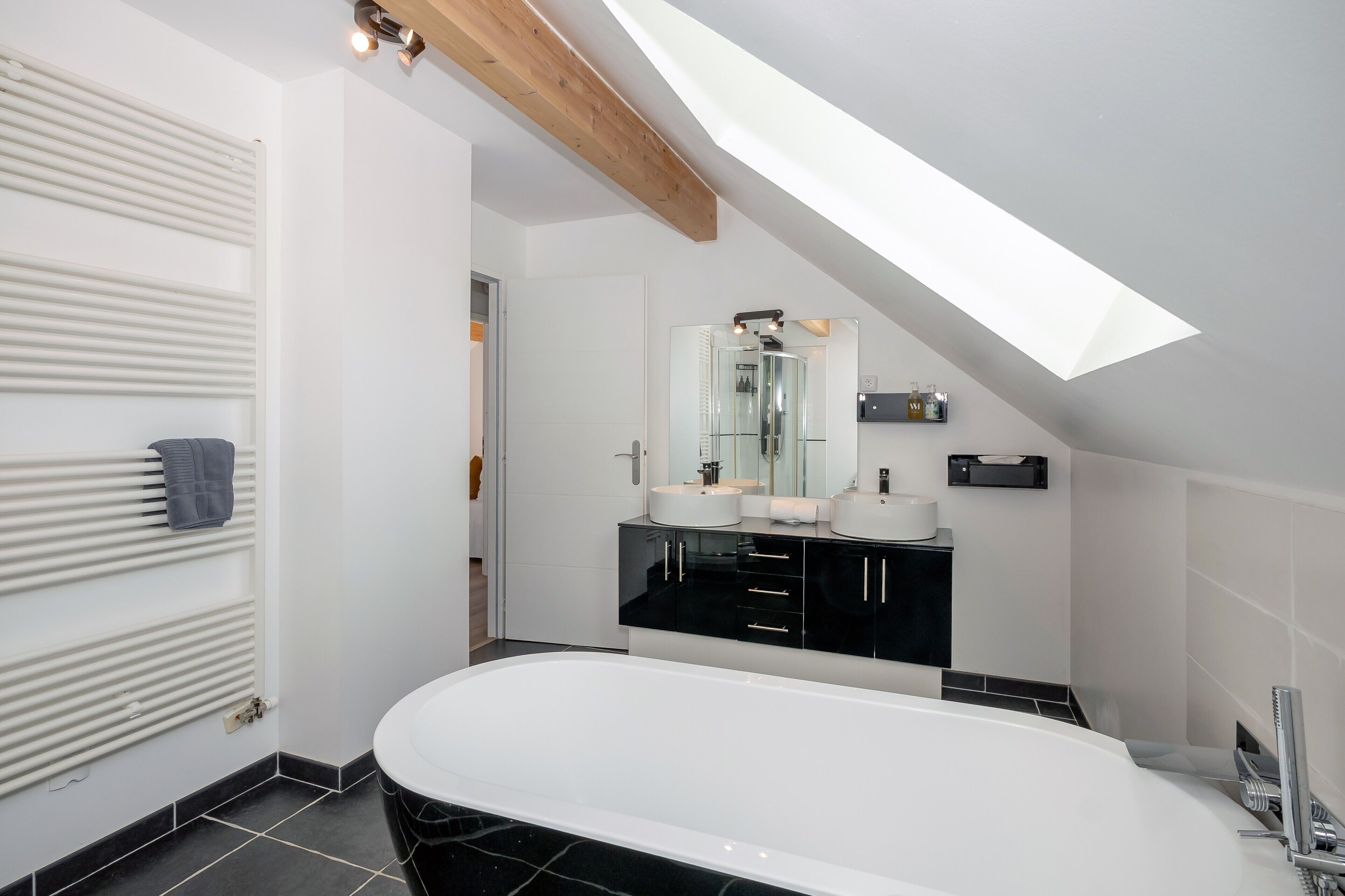 A modern bathroom with a freestanding bathtub, a large mirror, and a black vanity.