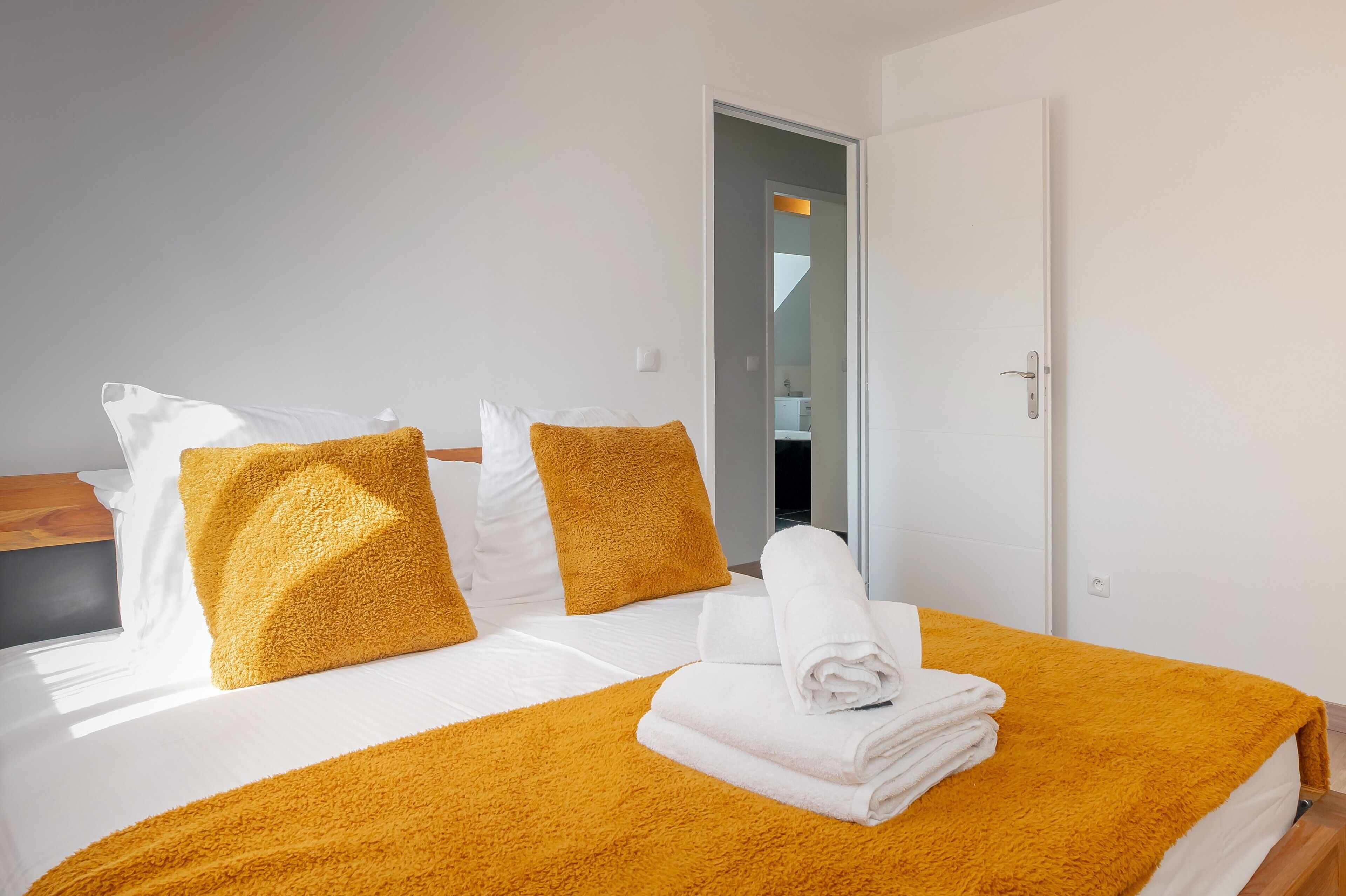 Una camera d'albergo con un letto, biancheria da letto bianca e una coperta gialla.