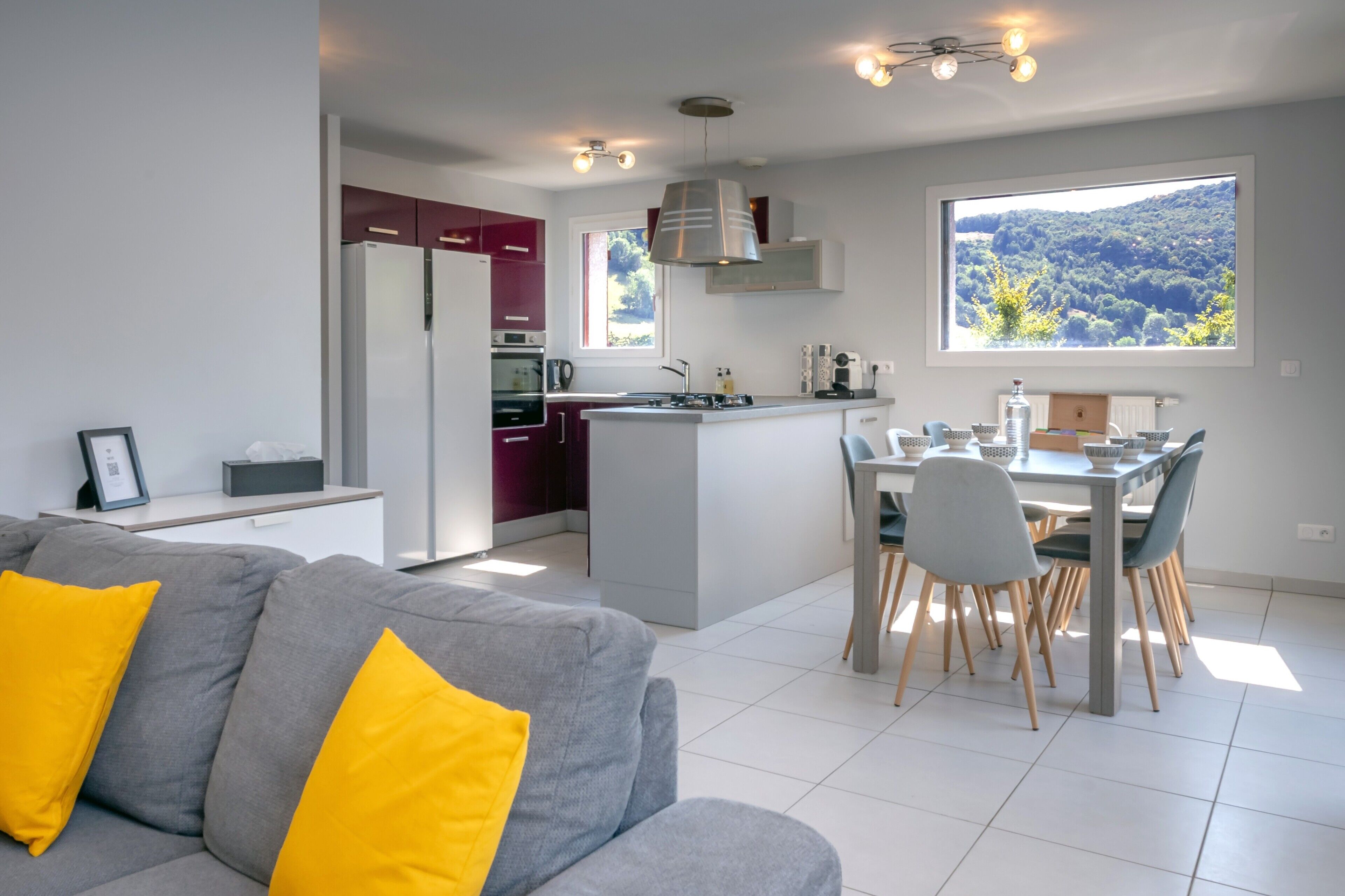 Een moderne keuken met een centraal eiland, een eethoek met stoelen, en een bank met gele kussens.