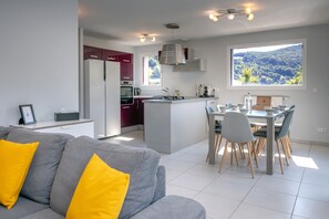 Una cocina moderna con una isla central, zona de comedor con sillas y un sofá con cojines amarillos.