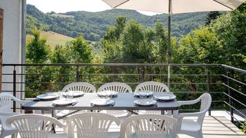 Une terrasse avec une table dressée pour quatre personnes, entourée de chaises blanches, donnant sur une vallée verdoyante.