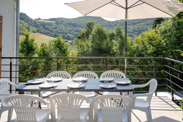 Una terraza con una mesa para cuatro, rodeada de sillas blancas, con vistas a un valle exuberante.