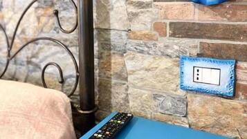 A bed with a metal headboard, a blue bedside table, a remote control, a wall-mounted light fixture, and a power outlet.