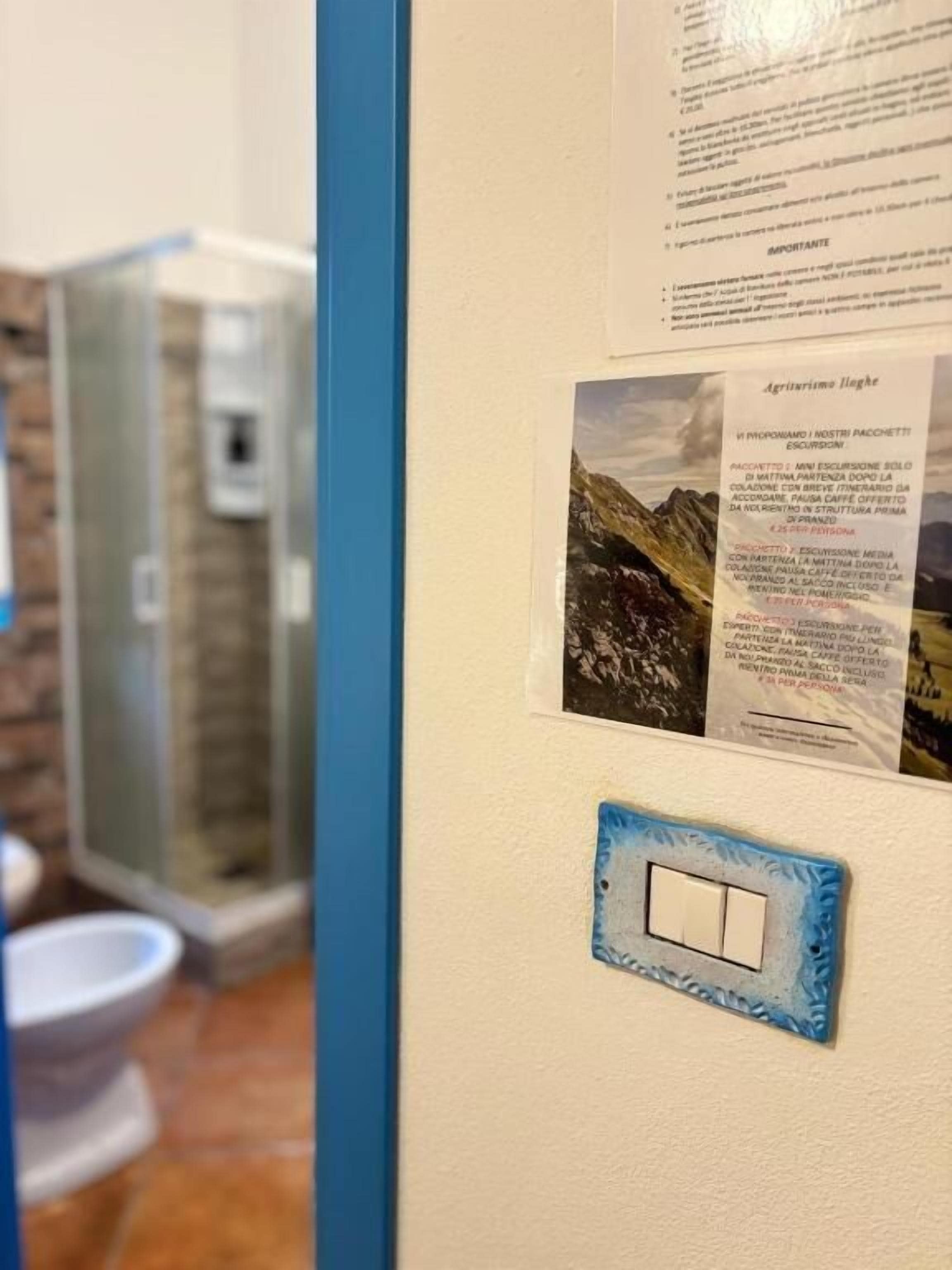 Une salle de bain avec une douche à parois de verre, des toilettes blanches et un interrupteur fixé au mur.