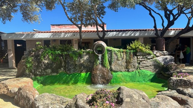 Un patio con jardín de rocas, fuente de agua y edificio con tejado de tejas rojas.